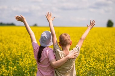 Elleri havada mutlu çocuklar. Çiçek açan sarı kolza tohumu tarlasında yazın tadını çıkarıyorlar.