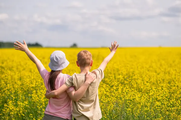 Kollarını kaldırmış anne ve oğlu sarı kolza tohumu tarlasında güneşli bir günün tadını çıkarıyorlar.