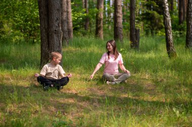 Anne ve oğlu orman çimlerinde bağdaş kurmuş, uyum içinde meditasyon yapıyorlar.