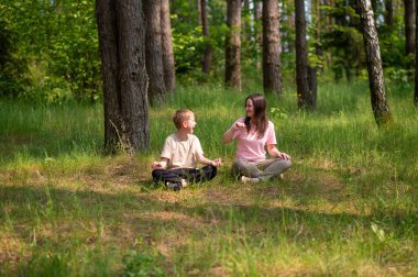 Anne ve oğlu nilüfer çiçekleri içinde meditasyon yapıyor ve gülüyor. Orman çayırlarında poz veriyor, birlikte doğanın ve zamanın tadını çıkarıyor.