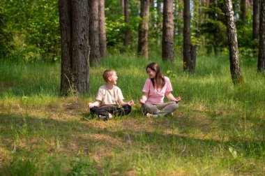 Anne ve oğlu nilüfer çiçekleri içinde meditasyon yapıyor ve gülüyor. Orman çayırlarında poz veriyor, birlikte doğanın ve zamanın tadını çıkarıyor.