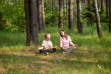 Anne ve oğlu nilüfer çiçekleri içinde meditasyon yapıyor ve gülüyor. Orman çayırlarında poz veriyor, birlikte doğanın ve zamanın tadını çıkarıyor.