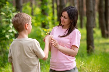 Güneşli bir ormanda annesine çiçek veren bir çocuk, doğada şefkatli bir aile anı.