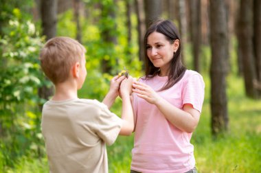 Güneşli bir ormanda annesine çiçek veren bir çocuk, doğada şefkatli bir aile anı.