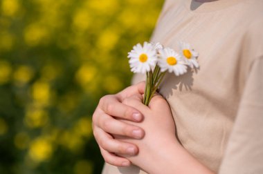 Çiçek açan sarı bir tarlada göğsüne papatya dolu bir demet papatya tutan çocuğun yakın çekimi, huzurlu bir yaz anıydı.