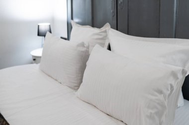 Modern bir otel odasında beyaz yastıklar ve çarşaflarla düzgünce yapılmış rahat ve temizliği sembolize ediyor.