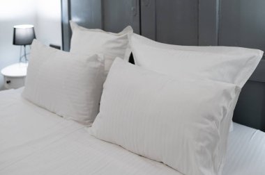 Modern bir otel odasında beyaz yastıklar ve çarşaflarla düzgünce yapılmış rahat ve temizliği sembolize ediyor.