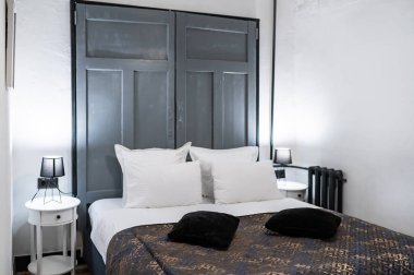 Koyu yatak örtüsü ve beyaz yastıkları olan otel yatağı, rahat bir odada zarif ve davetkar bir atmosfer.