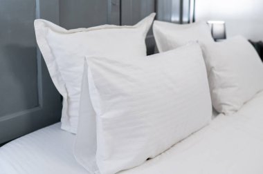 Otel odasında yumuşak beyaz yastık ve yastıklı yatak başlığı, temiz ve rahat bir atmosfer.