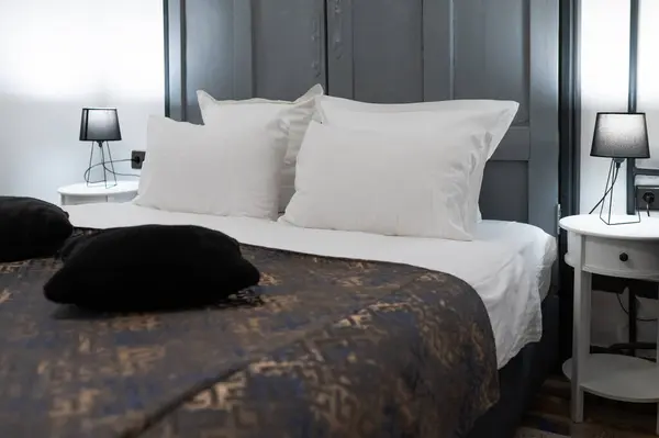 Koyu yatak örtüsü ve beyaz yastıkları olan otel yatağı, rahat bir odada zarif ve davetkar bir atmosfer.