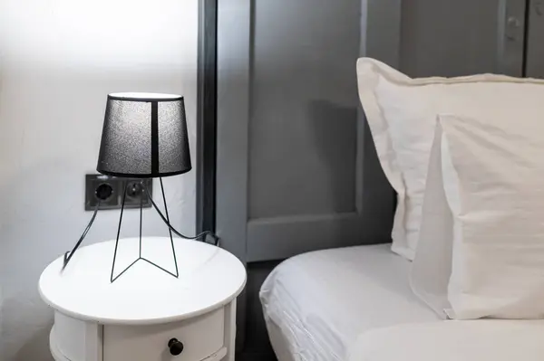 Modern otel odasındaki yatağın yanındaki beyaz masada siyah bir lamba.