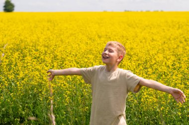 Sıcak bir yaz gününde canlı sarı bir kolza tohumu tarlasında gülümseyen ve rahatlatan genç sarışın çocuk.