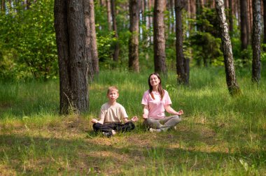 Anne ve oğlu nilüfer çiçekleri içinde meditasyon yapıyor ve gülüyor. Orman çayırlarında poz veriyor, birlikte doğanın ve zamanın tadını çıkarıyor.