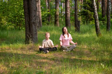 Anne ve oğlu orman çimlerinde bağdaş kurmuş, uyum içinde meditasyon yapıyorlar.