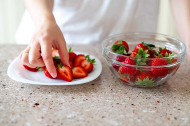 Sağlıklı atıştırmalıklar hazırlarken iki tabak dilimlenmiş çilek ve bütün çilek tutan kadın ellerini kapat.