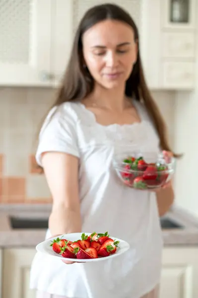 Parlak mutfakta iki tabak taze çilek tutan kadın, tabağa odaklan.