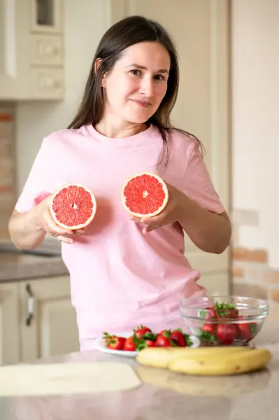 Neşeli kadın, sağlıklı beslenme ve yaşam tarzını geliştirmek için göğsünde greyfurt yarıları gösteriyor.