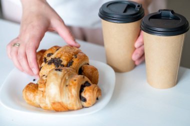 Evde elinde kruvasan ve kahve fincanı tutan bir kadın, basit zevklerin tadını çıkarıyor.