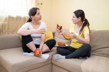İki kadın kanepede oturuyor, konuşuyor, gülüyor, atıştırmalık ve içeceklerden hoşlanıyor, boş zaman ve arkadaşlık kavramı.