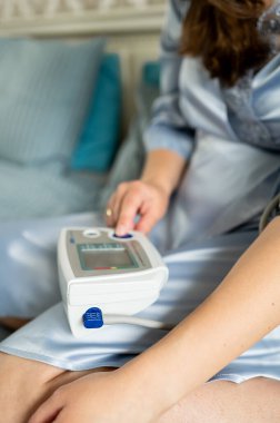 Kadın dijital tansiyon monitöründe düğmeye basıyor, sağlık kontrolüne başlıyor, kendini izleme ve ev sağlığı konsepti