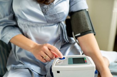 Kadın dijital tansiyon monitöründe düğmeye basıyor, sağlık kontrolüne başlıyor, kendini izleme ve ev sağlığı konsepti