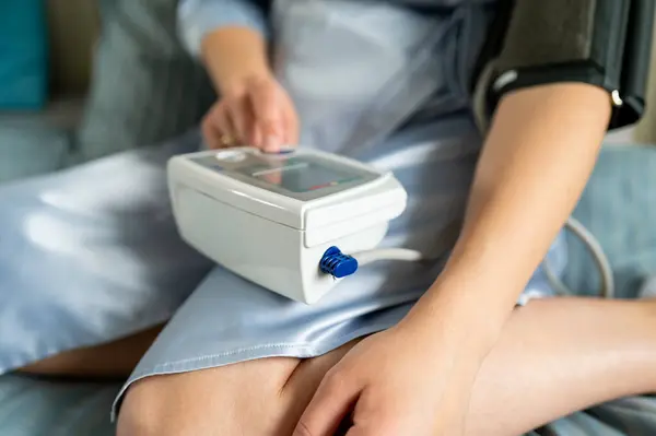 Kadın dijital tansiyon monitöründe düğmeye basıyor, sağlık kontrolüne başlıyor, kendini izleme ve ev sağlığı konsepti