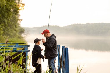 Baba, gölün kenarındaki sisli bir sabahta oğluna yardım ediyor. Huzurlu bir bağ kurma anında sabır ve özen gösteriyor.