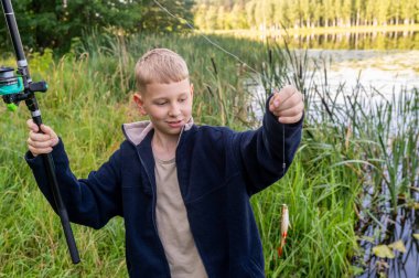 Neşeli çocuk, bir yaz günü doğada başarılı bir balık avladıktan sonra gururla küçük balıkları tutuyor.