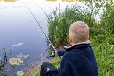 Genç bir çocuk bir yaz günü nehir kenarında balık tutuyor, açık hava ve kırsal atmosferin tadını çıkarıyor.