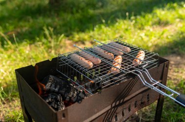 Lezzetli sosisler portatif ızgarada kızartılıyor yaz günü aile içinde balık tutma gezisi sırasında.