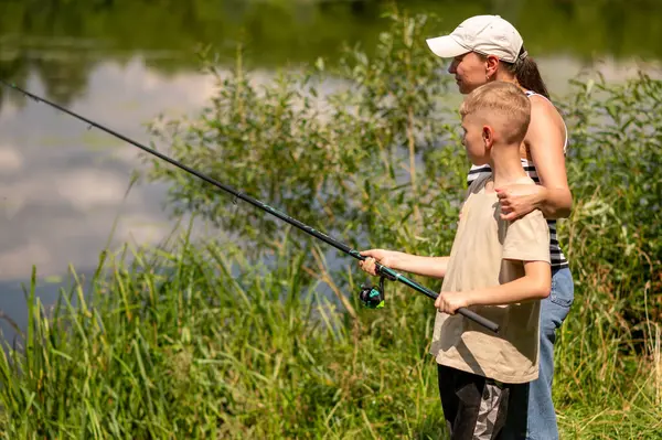  Anne ve genç oğul güneşli bir yaz gününde gölde balık tutuyor, kaynaşıyor, dışarıda dinleniyor, doğanın tadını çıkarıyor, huzurlu su manzaraları ve kaliteli aile zamanları.