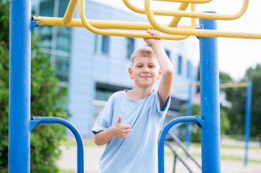 Parktaki maymun barlarının yanındaki neşeli sarışın çocuk gülümsüyor ve güneşli bir günde açık havada oynamaktan zevk alıyor.