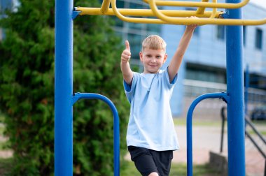 Parktaki maymun barlarının yanındaki neşeli sarışın çocuk gülümsüyor ve güneşli bir günde açık havada oynamaktan zevk alıyor.