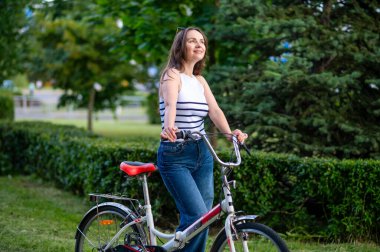 Neşeli kadın bisikletle güneşli parkta duruyor aktif yaşam tarzının ve doğanın, sağlığın, mutluluğun ve rahatlama konseptinin tadını çıkarıyor.