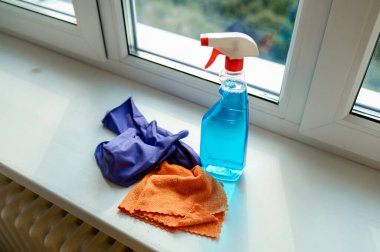 Pencere kenarına yerleştirilmiş sprey, bez ve eldivenler pencere temizleme ve ev işleri için hazırlanıyor.