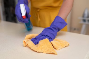 Eldiven giyen bir kadın mobilya cilası sıkar ve dikkatli bir şekilde ahşap bir masayı bezle siler, evde bakım ve bakım üzerine odaklanır.