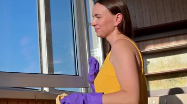 Genç bir kadın, balkon penceresini parlak güneş ışığında yıkıyor, evdeki temiz havayı ve temiz havayı koruyor.