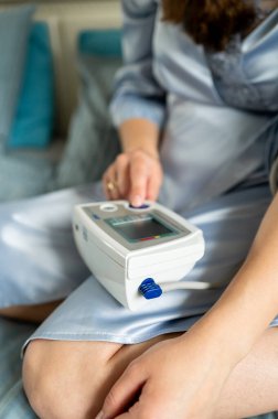 Kadın dijital tansiyon monitöründe düğmeye basıyor, sağlık kontrolüne başlıyor, kendini izleme ve ev sağlığı konsepti