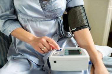 Kadın dijital tansiyon monitöründe düğmeye basıyor, sağlık kontrolüne başlıyor, kendini izleme ve ev sağlığı konsepti