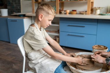 Çocuk ve kadın eğitmen çömlek çarkında birlikte kil şekillendiriyorlar, çocuklar geleneksel zanaat öğreniyorlar.