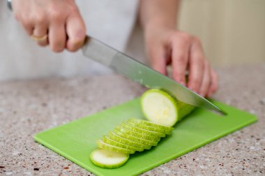 Yeşil bir tahtada kabak dilimleyen ellerin yakın çekimi, kavram: evde taze yemek hazırlığı