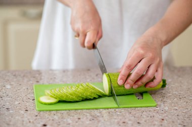 Yeşil bir tahtada kabak dilimleyen ellerin yakın çekimi, kavram: evde taze yemek hazırlığı