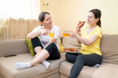 İki kadın kanepede oturuyor, konuşuyor, gülüyor, atıştırmalık ve içeceklerden hoşlanıyor, boş zaman ve arkadaşlık kavramı.