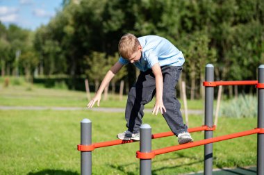 Açık hava spor sahasında paralel barlarda duran genç çocuk, spor konsepti, egzersiz, güç, aktif yaşam tarzı ve yaz etkinliği.