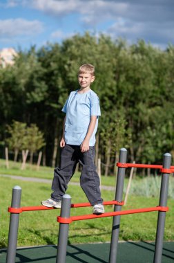 Açık hava spor sahasında paralel barlarda duran genç çocuk, spor konsepti, egzersiz, güç, aktif yaşam tarzı ve yaz etkinliği.