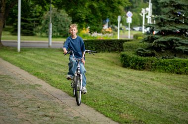 Sıcak bir yaz gününde yeşil parkta bisiklet süren neşeli sarışın çocuk, doğanın, özgürlüğün ve açık havada eğlencenin tadını çıkarıyor.