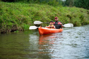 Baba ve oğul güneşli bir yaz gününde sakin bir nehirde kanoya biniyor, aile bağlarının, açık hava maceralarının, su sporlarının ve doğanın tadını çıkarıyorlar.