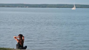 Antrenmandan sonra büyük göl kenarında oturan bir kadın. Uzakta yelkenli teknesi var.