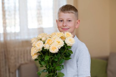 Genç çocuk, Anneler Günü 'nde aşkını, minnettarlığını ve aile bağlarını kutlamak için annesine hediye etmeye hazır canlı sarı bir gül buketi tutuyor.