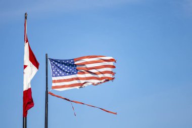 Yıpranmış ve parçalanmış bir Amerikan Bayrağı Kanada Bayrağı 'nın yanında rüzgarda dalgalanıyor.